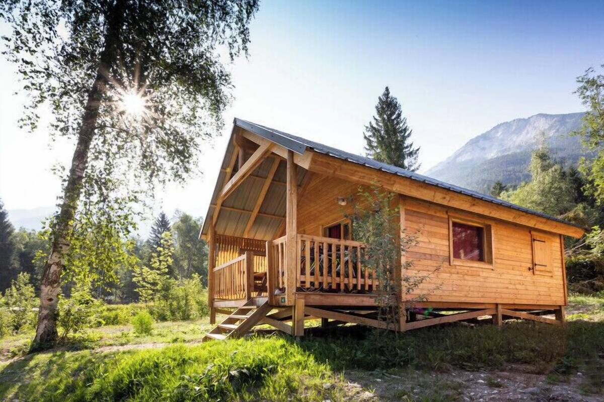 Eine Holzchalet mit Balkon, eingebettet in einen bewaldeten Bereich mit Bergen im Hintergrund.