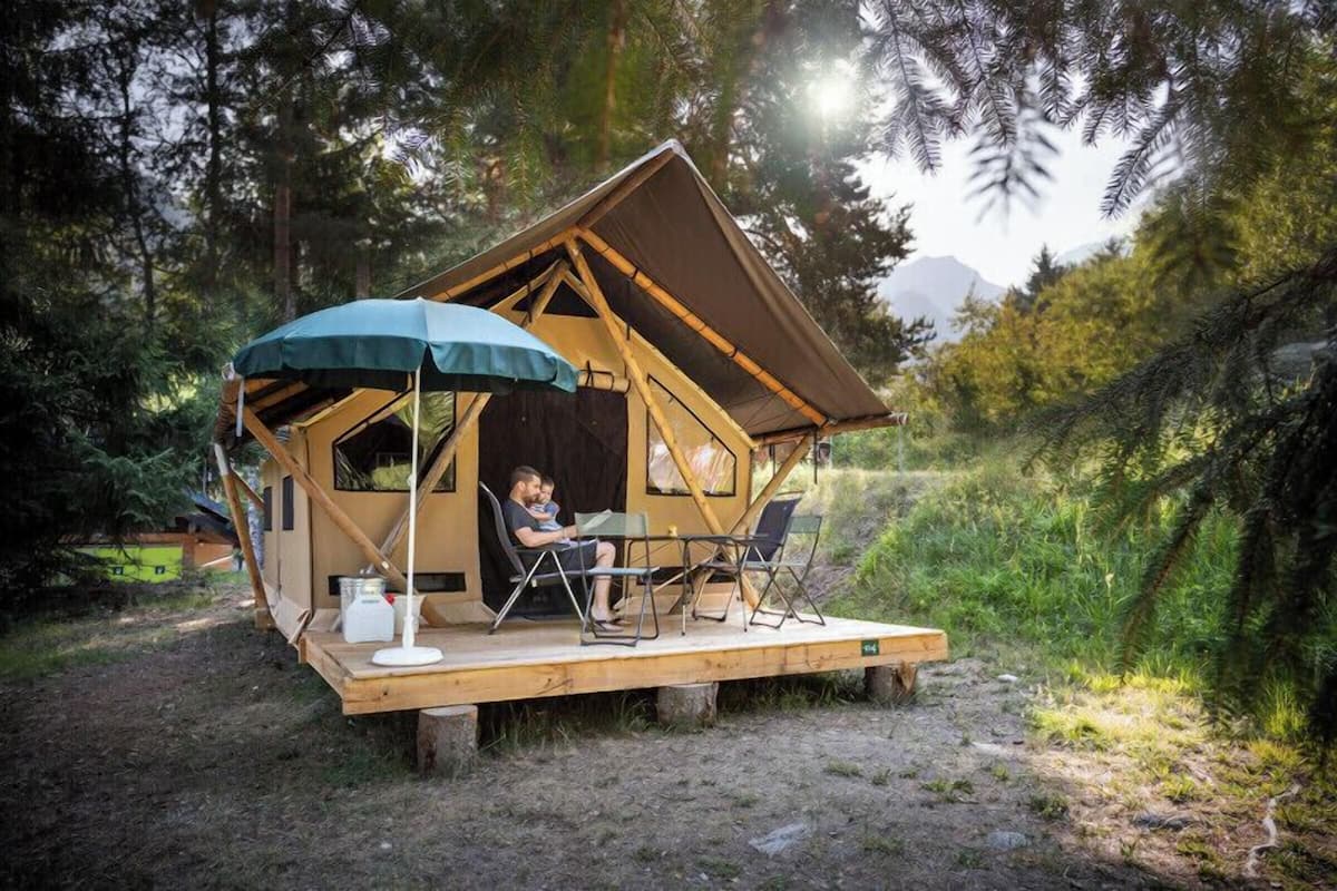 Eine kleine, hölzerne Hütte mit Veranda, Tisch und Stühlen, umgeben von Bäumen.