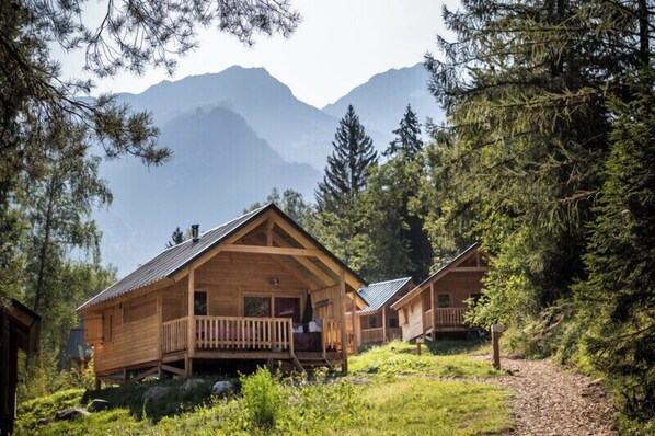 A wooden cabin with a porch, surrounded by trees and mountains.