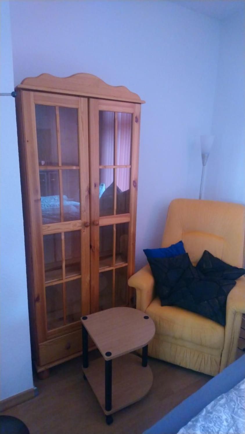 A room with a wooden cabinet, a small table, and a yellow armchair with cushions.