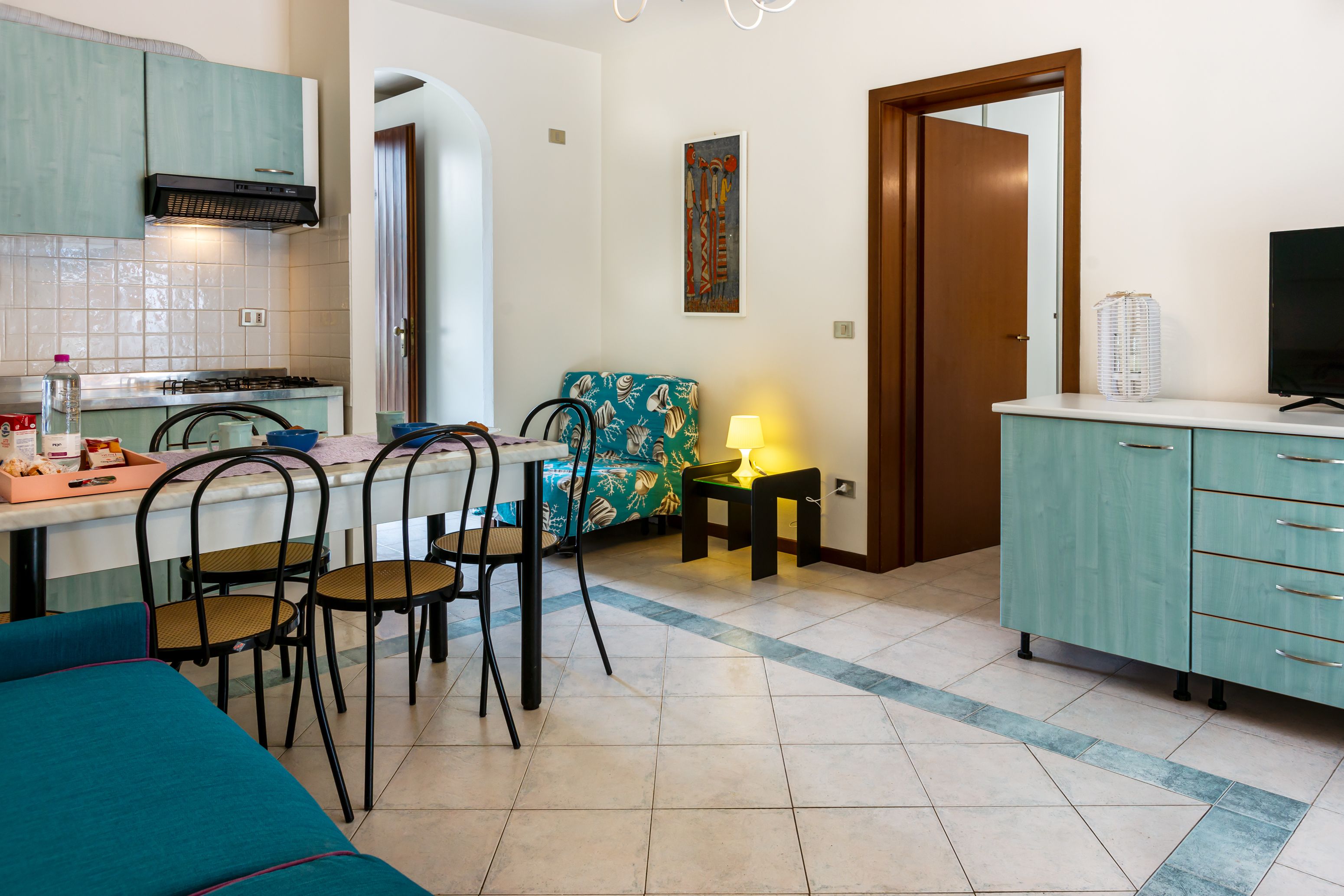 A compact kitchen with a dining area, a sofa, and a TV.