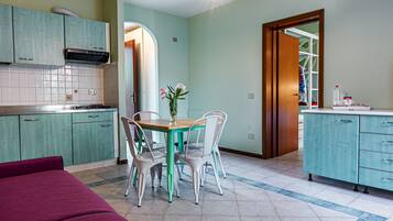 A compact kitchen with teal cabinets, a dining table with chairs, and a visible door leading to another room.