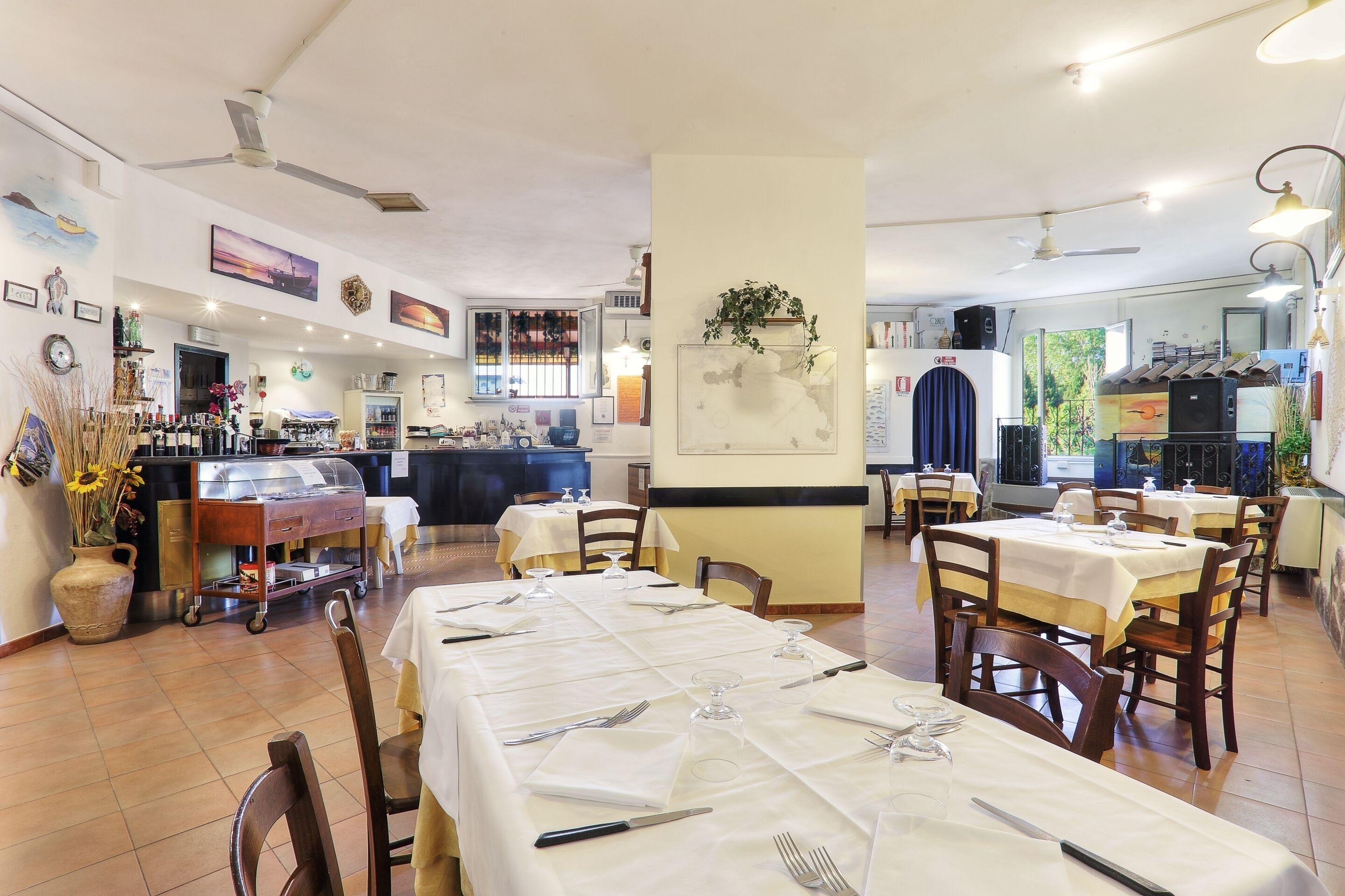 Un ristorante con tavoli apparecchiati per consumare, una zona bar e un bancone con prodotti alimentari.