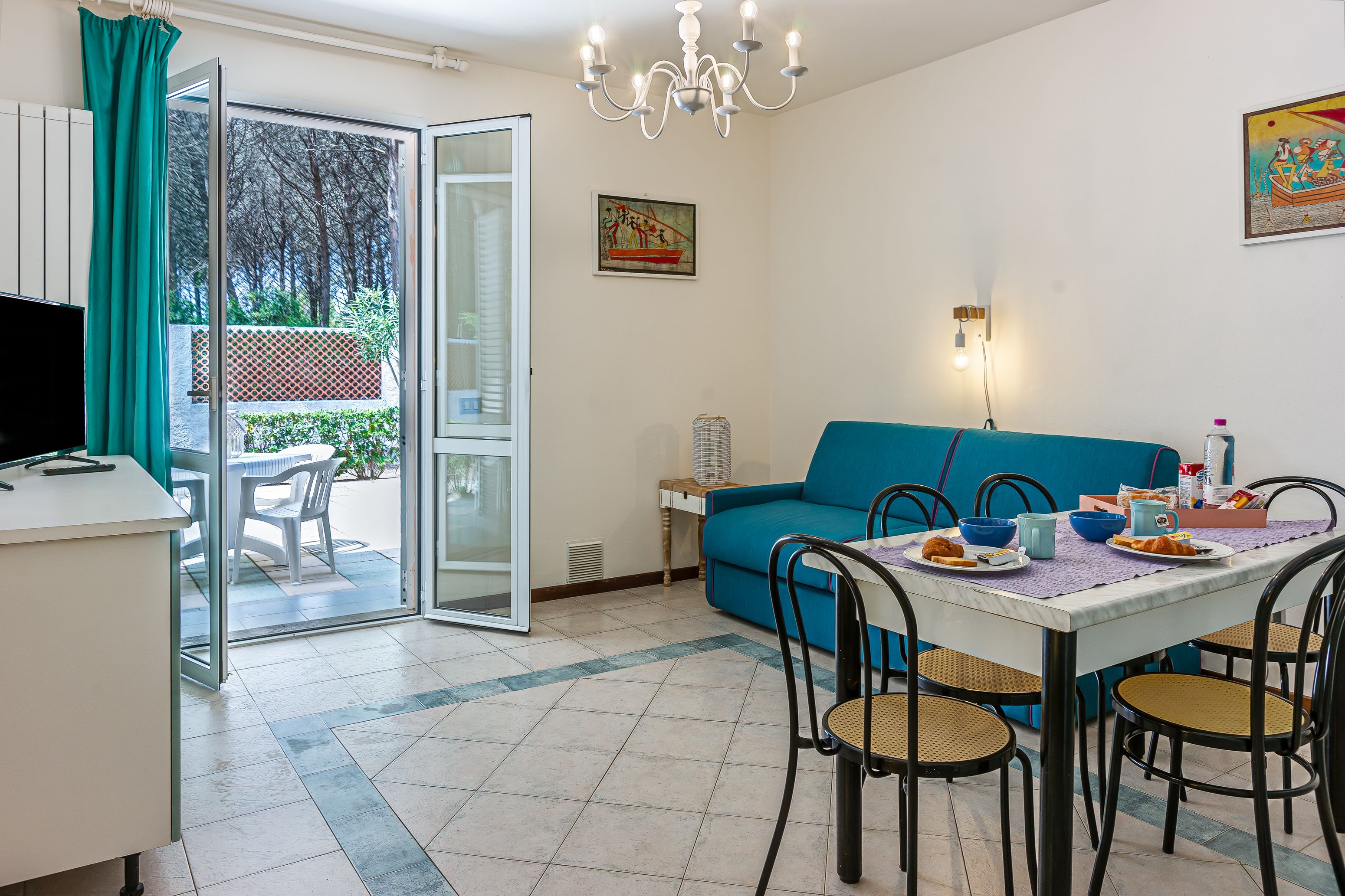 A dining area with a table set for four, a blue sofa, and a television on a desk.