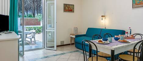 A dining area with a table set for four, a blue sofa, and a television on a desk.