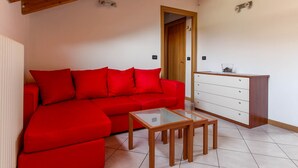 A red sofa, a glass-top coffee table, and a wooden dresser in a room with white walls and a wooden ceiling beam. - Barcaiolo Apartment (Lecco)