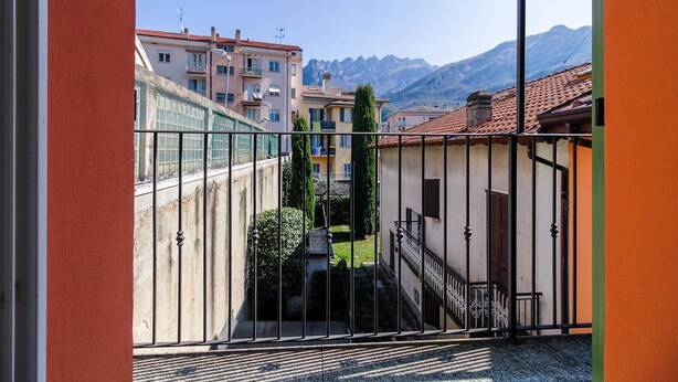 A view from a balcony overlooking a courtyard with buildings and mountains in the background. - Barcaiolo Apartment (Lecco)