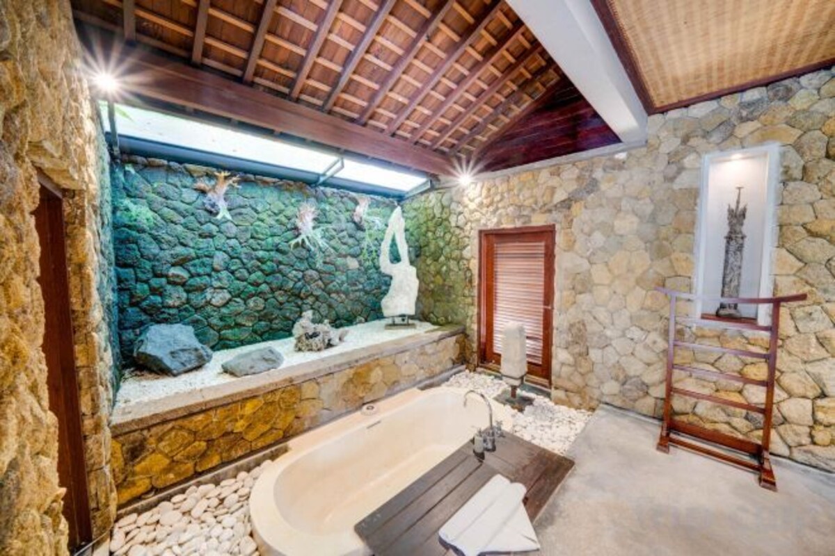 Un baño con pared de piedra, una bañera y un estante de madera.