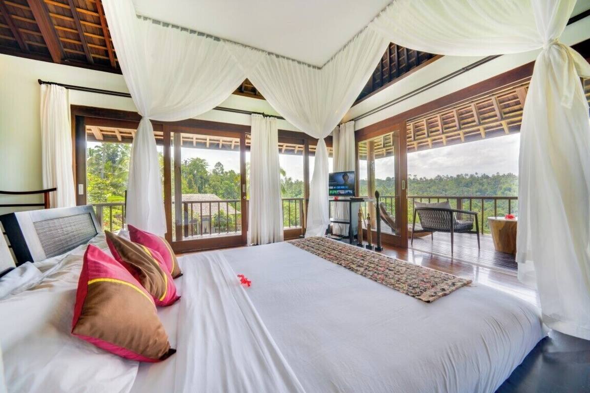A bedroom with a large bed, white curtains, and a view of the outdoors.