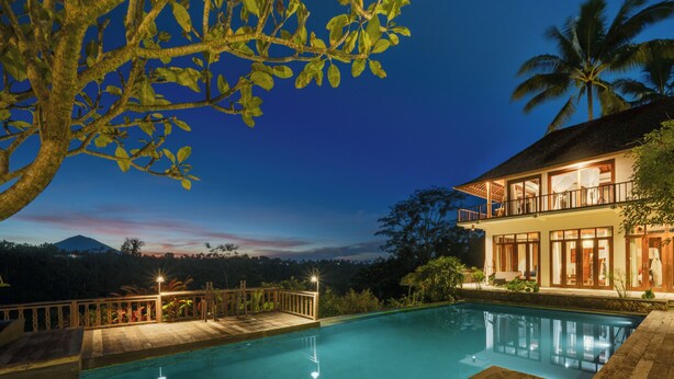 A swimming pool with a wooden deck, a wooden fence, and a building with large windows and a balcony. - Awan Putih Resort (Kerta)