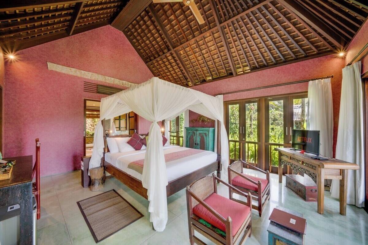A bedroom with a canopy bed, a desk with a television, and a view of greenery outside.