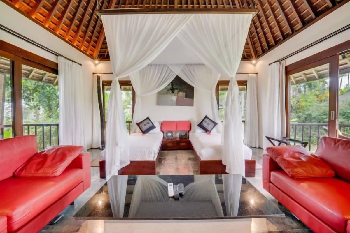 A room with a canopy bed, red sofas, and a glass coffee table.