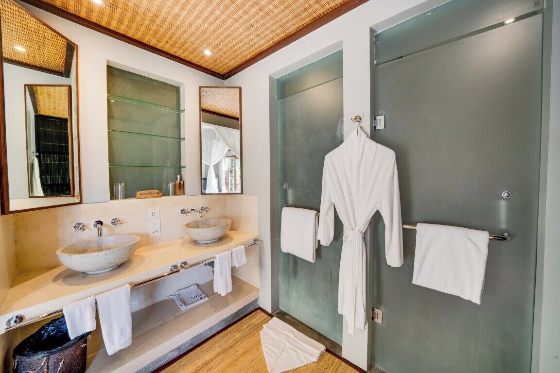 A modern bathroom with two sinks, a large mirror, a glass shower enclosure, and a robe hanging on the wall.