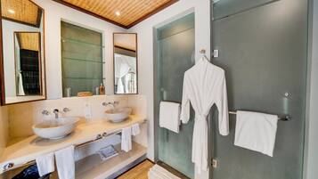 A modern bathroom with two sinks, a large mirror, a glass shower enclosure, and a robe hanging on the wall.