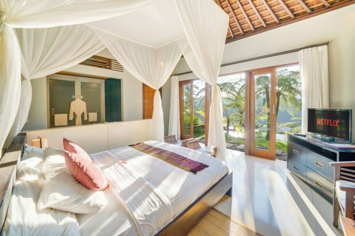A bedroom with a bed, a TV, and a view of palm trees.