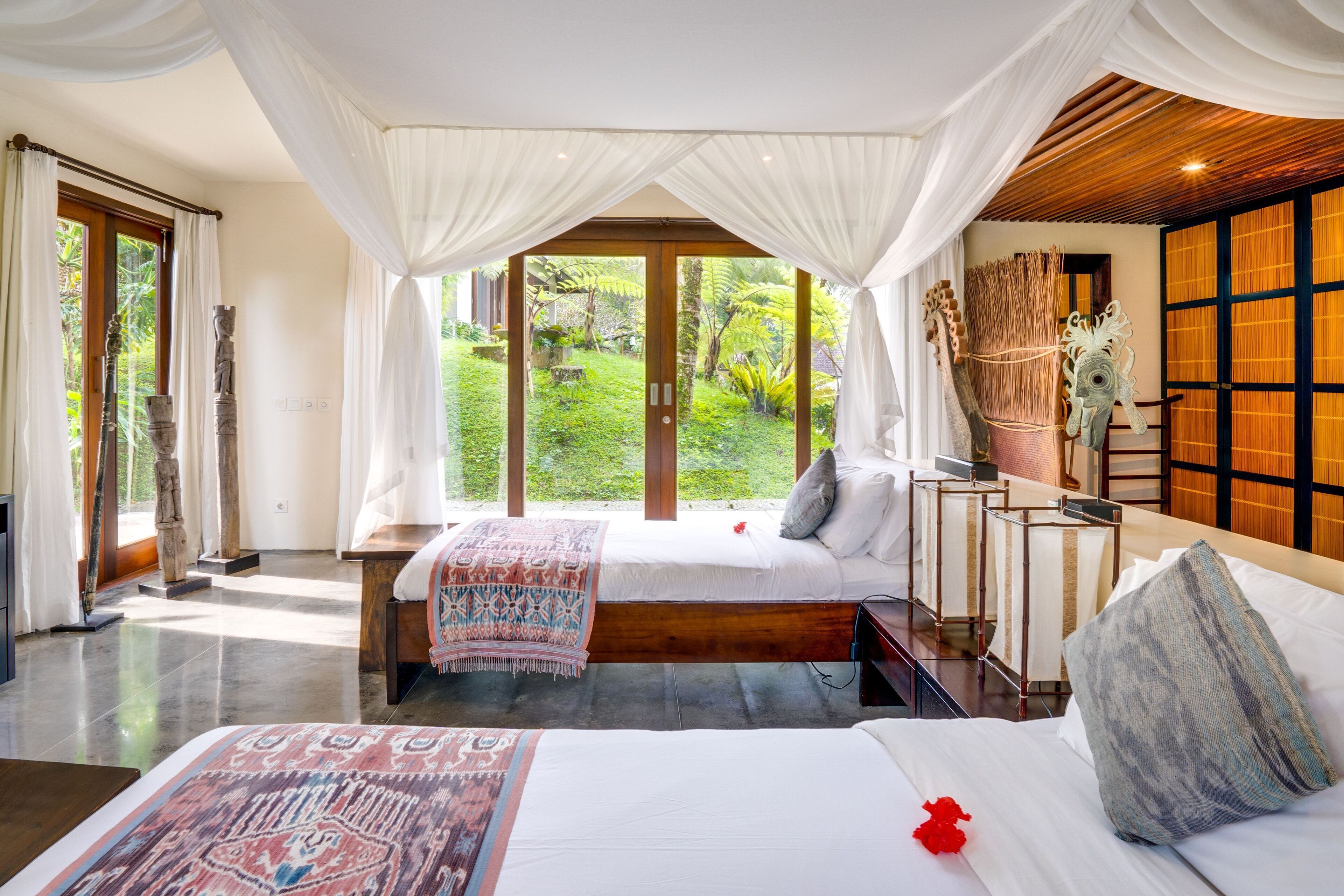 A bedroom with a large bed, a bench, and a view of a lush garden.