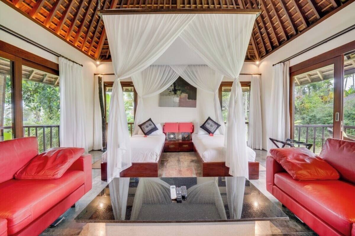 A room with a glass coffee table, two red leather sofas, a canopy bed with white bedding, and a painting on the wall.