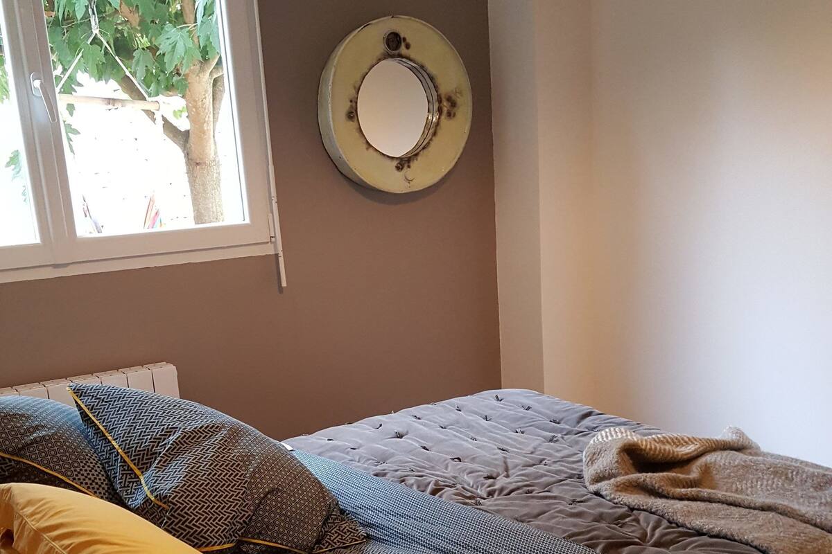 A bedroom with a bed, pillows, a window, and a wall-mounted mirror.