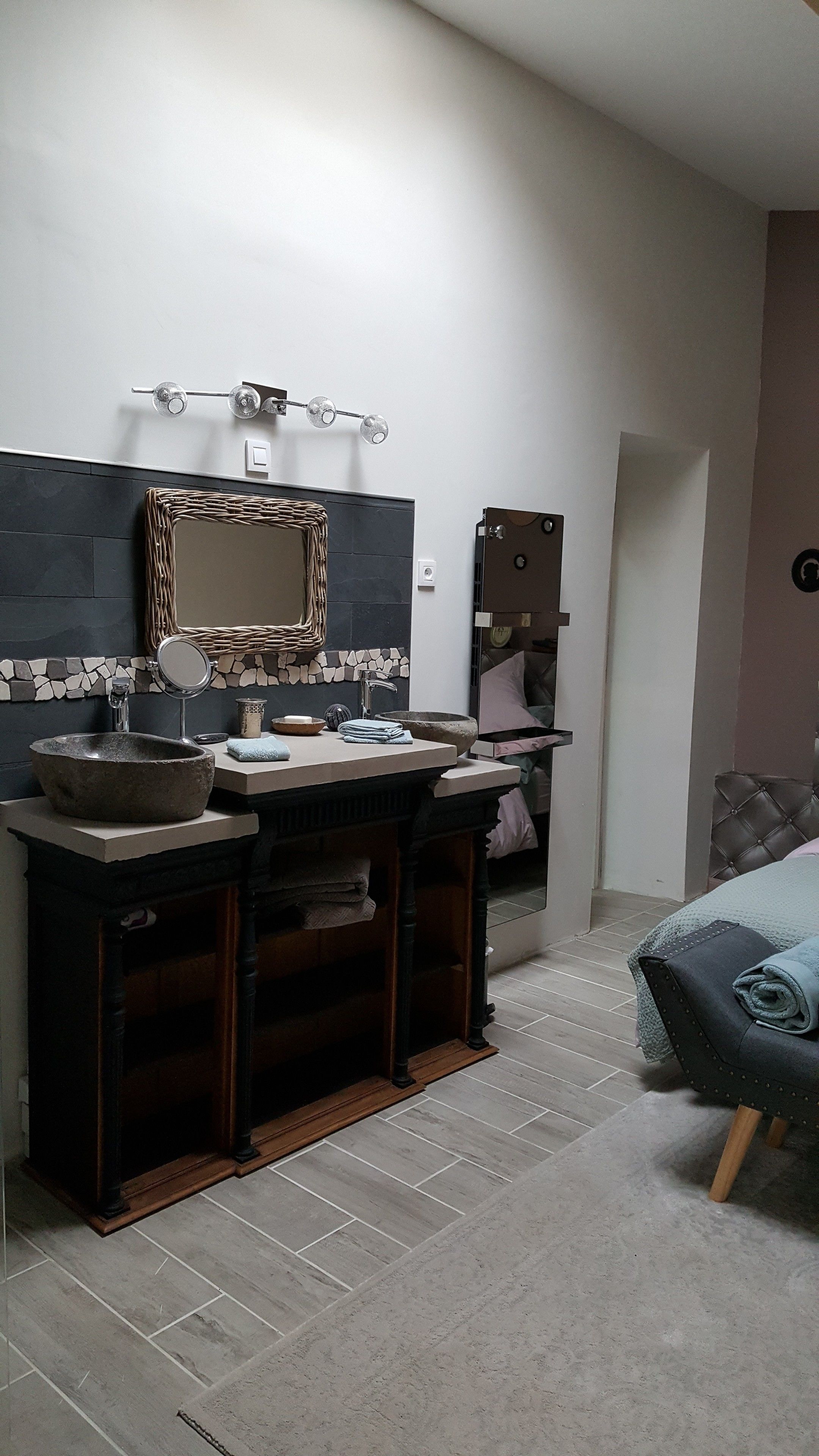 A bathroom with a stone sink, a mirror, a towel rack, and a vanity with a stool.