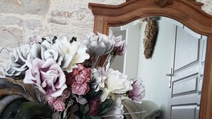 Une pièce avec un mur en pierre, un miroir doté d’un cadre en bois ouvragé et un arrangement floral dans un vase.