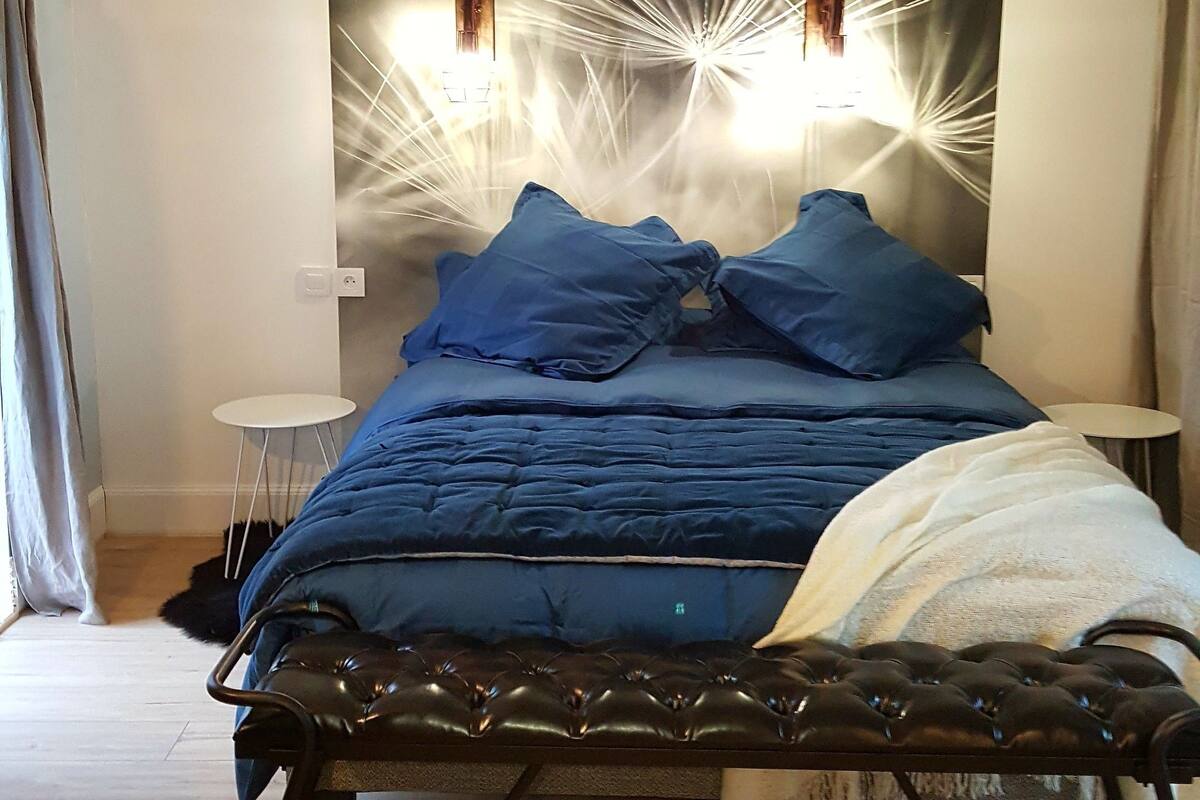 A modern bedroom with a bed, a small round table, and a wall-mounted light fixture.