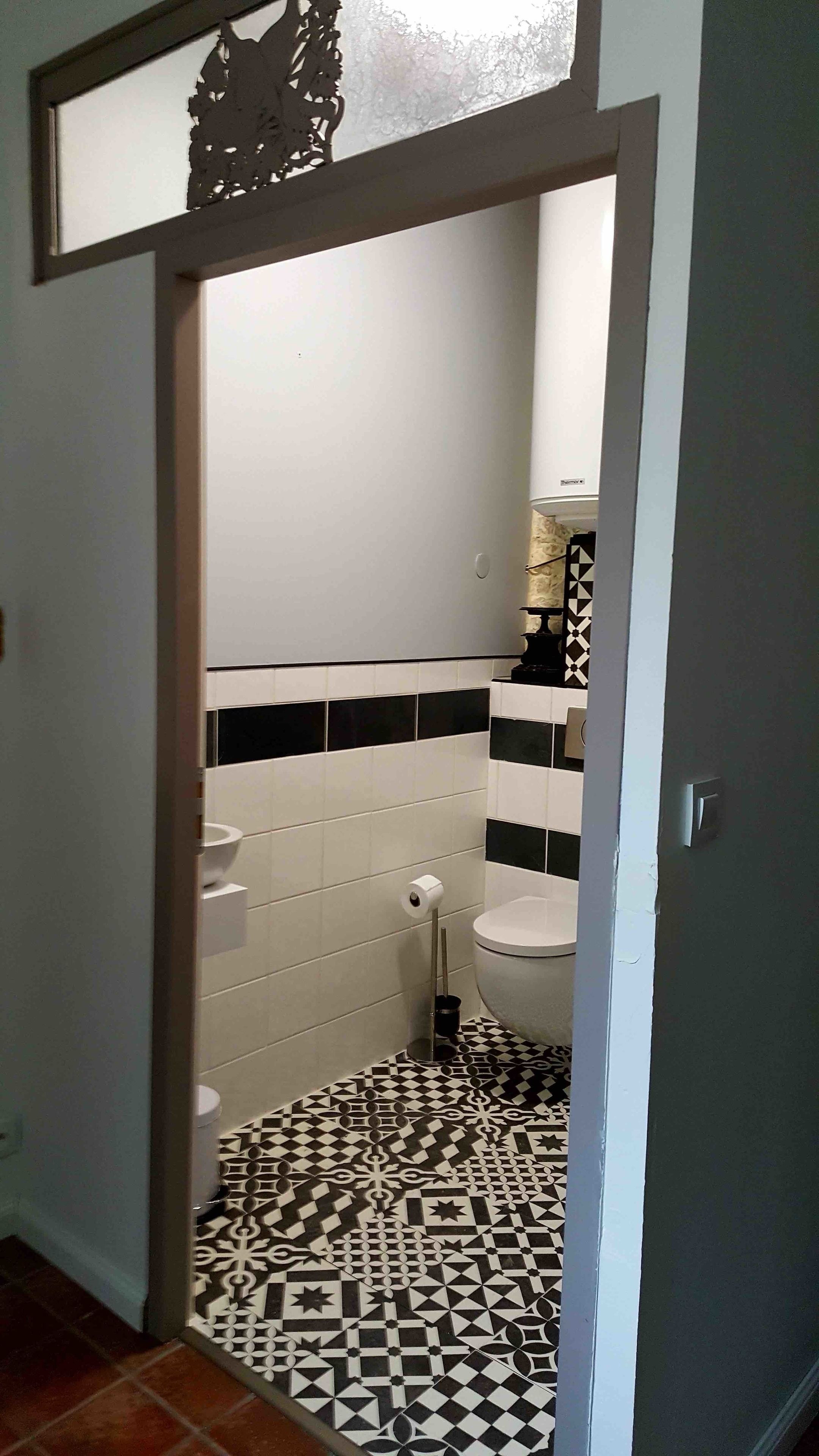 Une salle de bain avec un carrelage noir et blanc à motifs, des carreaux blancs sur les murs et des toilettes dotées d’un distributeur de savon noir et blanc à motifs.