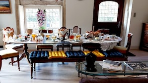 Un coin repas avec une table mise pour le petit-déjeuner, comprenant du pain, des œufs et des boissons. Des chaises sont disposées autour de la table, ainsi qu’un banc avec des coussins.