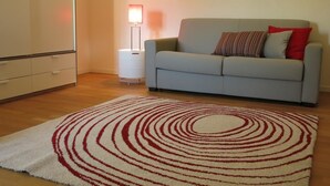 A living room with a grey sofa, a red and white patterned rug, and a floor lamp. - Appartamento Renzo (Lecco)
