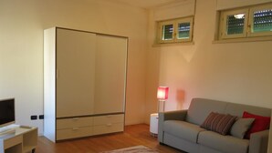 A modern living room with a sofa, a TV on a stand, a wardrobe, a lamp, and a patterned rug. - Appartamento Renzo (Lecco)