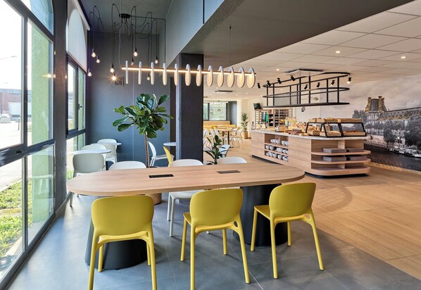 A modern interior with a central wooden table, yellow chairs, and a bar area with display cases.