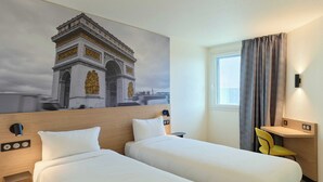 A hotel room with two beds, a desk, a chair, a painting of the Arc de Triomphe, and a window with curtains. - B&B HOTEL Paris Vitry-sur-Seine 3 étoiles (Vitry-sur-Seine)
