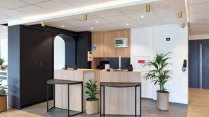 A reception area with a counter, two round tables, a dark-colored wardrobe, a small plant, and a potted plant. - B&B HOTEL Paris Vitry-sur-Seine 3 étoiles (Vitry-sur-Seine)