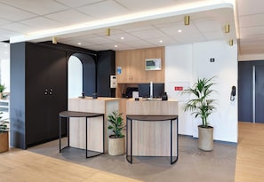 En receptionsdisk, to runde borde, et mørkt skab, en lille plante og en potteplante.