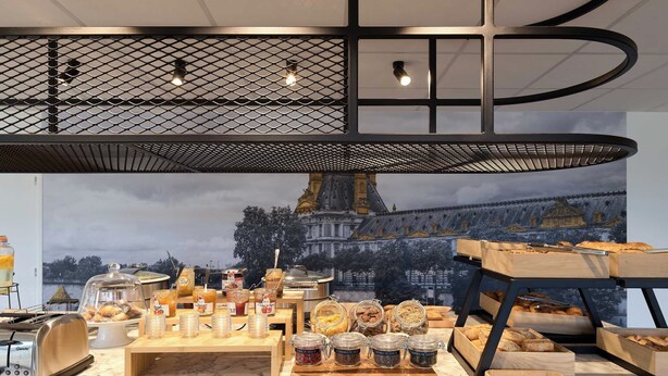 A breakfast buffet with various food items and condiments, a toaster, and a large window with a view of a building. - B&B HOTEL Paris Vitry-sur-Seine 3 étoiles (Vitry-sur-Seine)