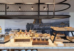 A breakfast buffet with various food items and condiments, a toaster, and a large window with a view of a building. - B&B HOTEL Paris Vitry-sur-Seine 3 étoiles (Vitry-sur-Seine)