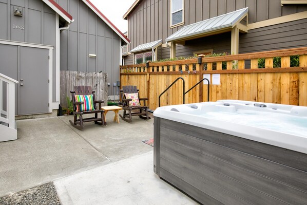 Un jardin avec un jacuzzi, une terrasse en bois et deux fauteuils Adirondack.