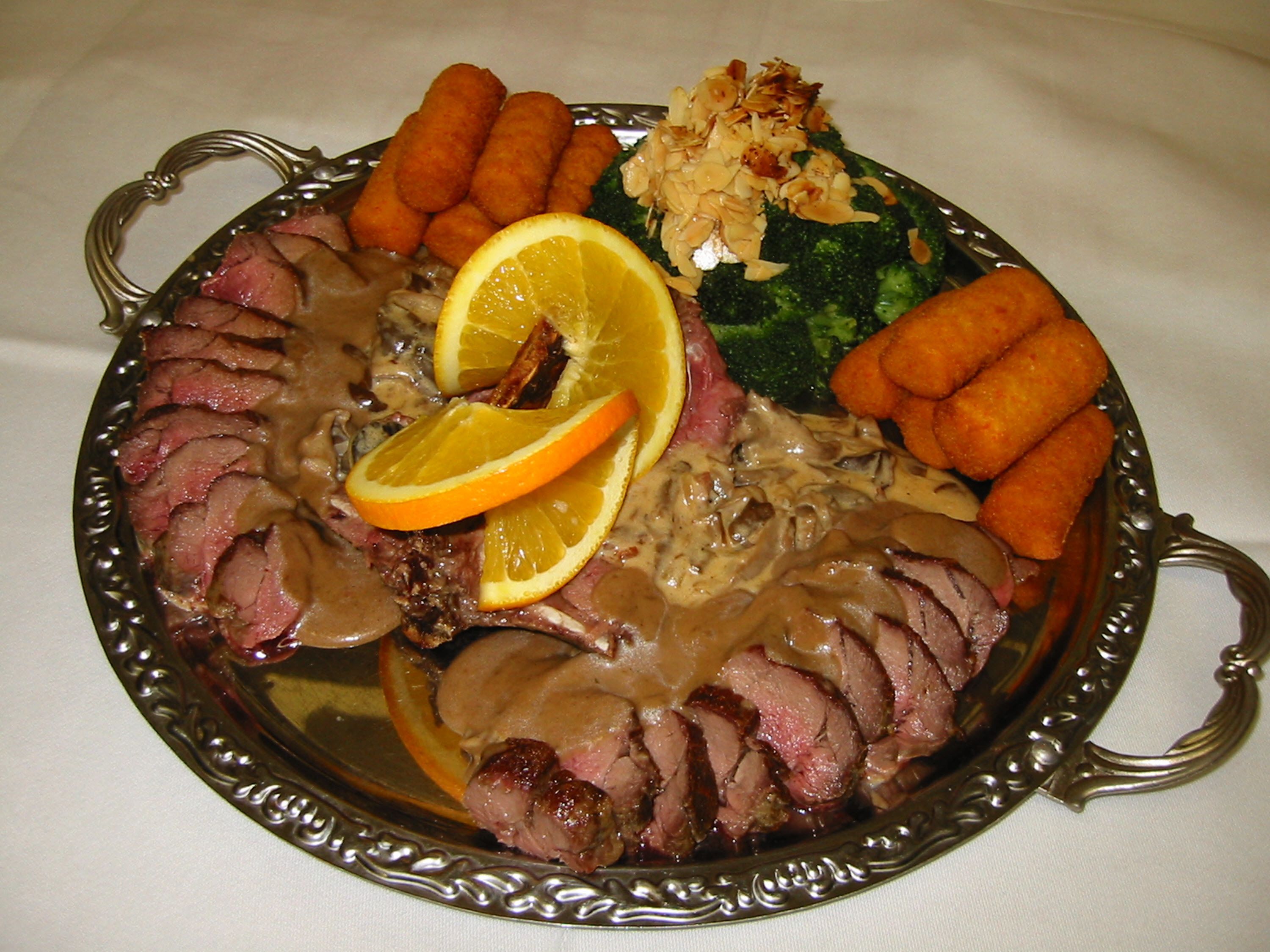 Un plato de comida con carne en rodajas, gajos de naranja y verduras.