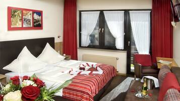 Ein Hotelzimmer mit einem Bett, einer rot-weiß gestreiften Tagesdecke, einem Strauß roter und weißer Rosen, einem roten Sessel, einem Tisch mit einer Champagnerflasche und einem roten Vorhang.