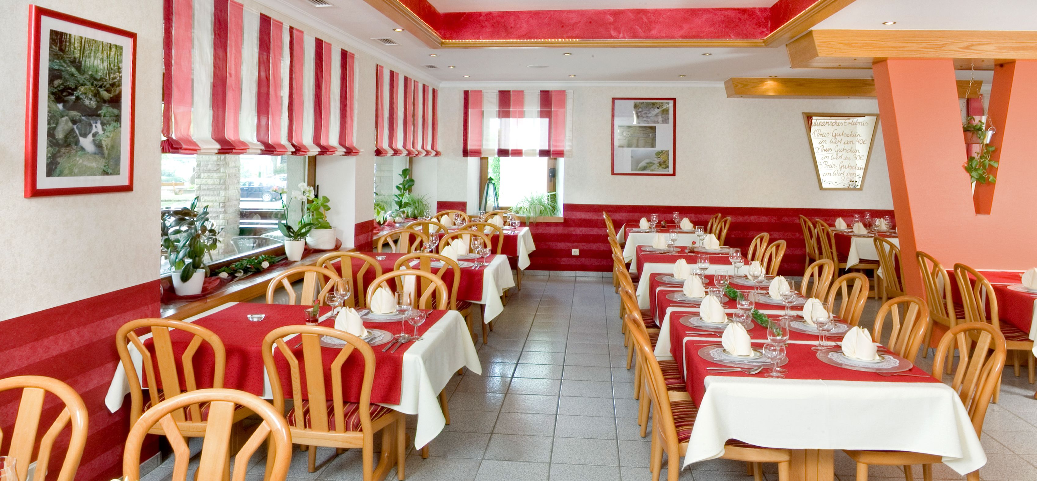 A restaurant with red and white striped curtains, wooden chairs, and tables set for dining.