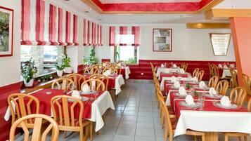 A restaurant with red and white striped curtains, wooden chairs, and tables set for dining.