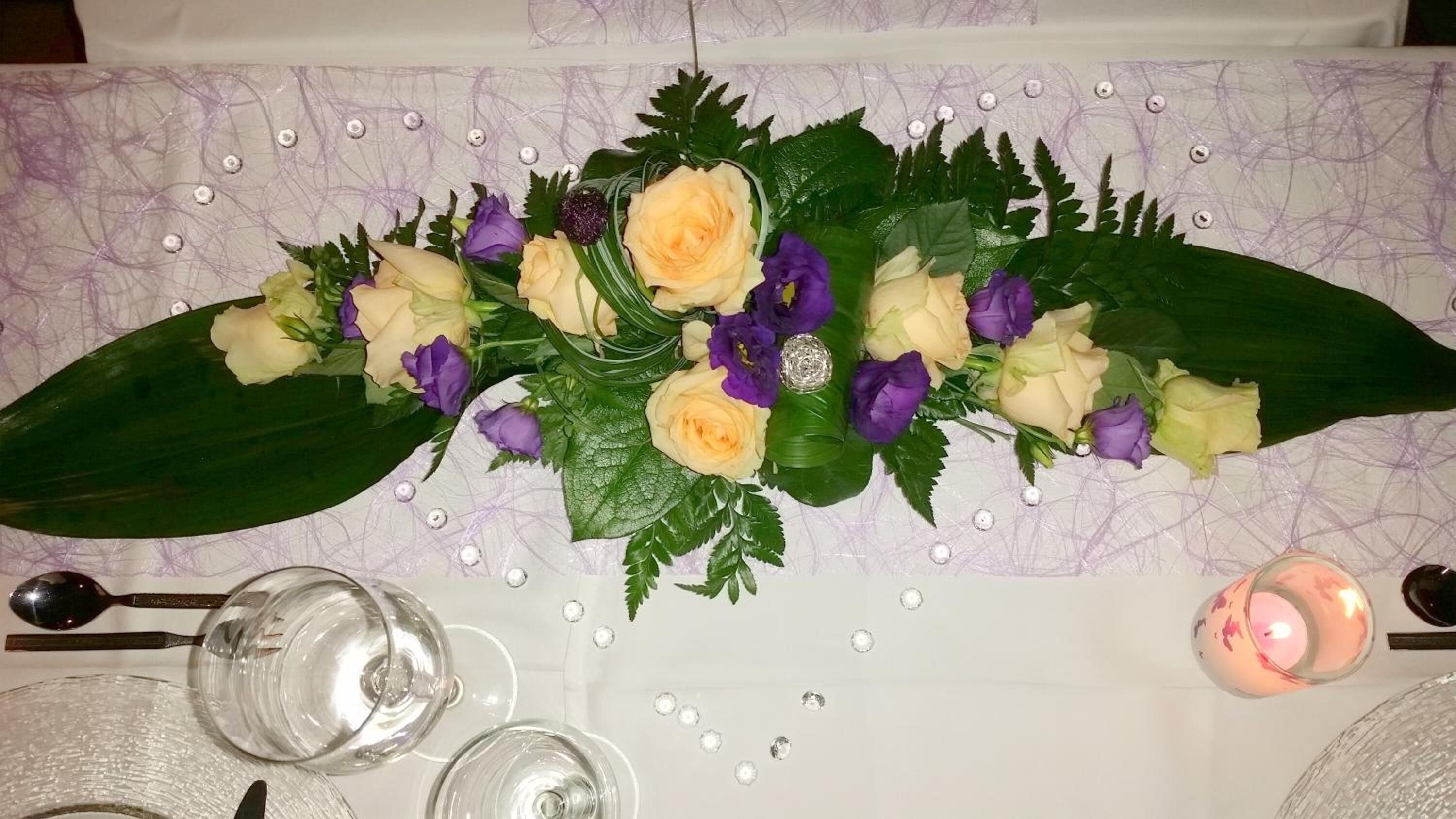 A table set with a floral centerpiece, clear glasses, and a pink candle.