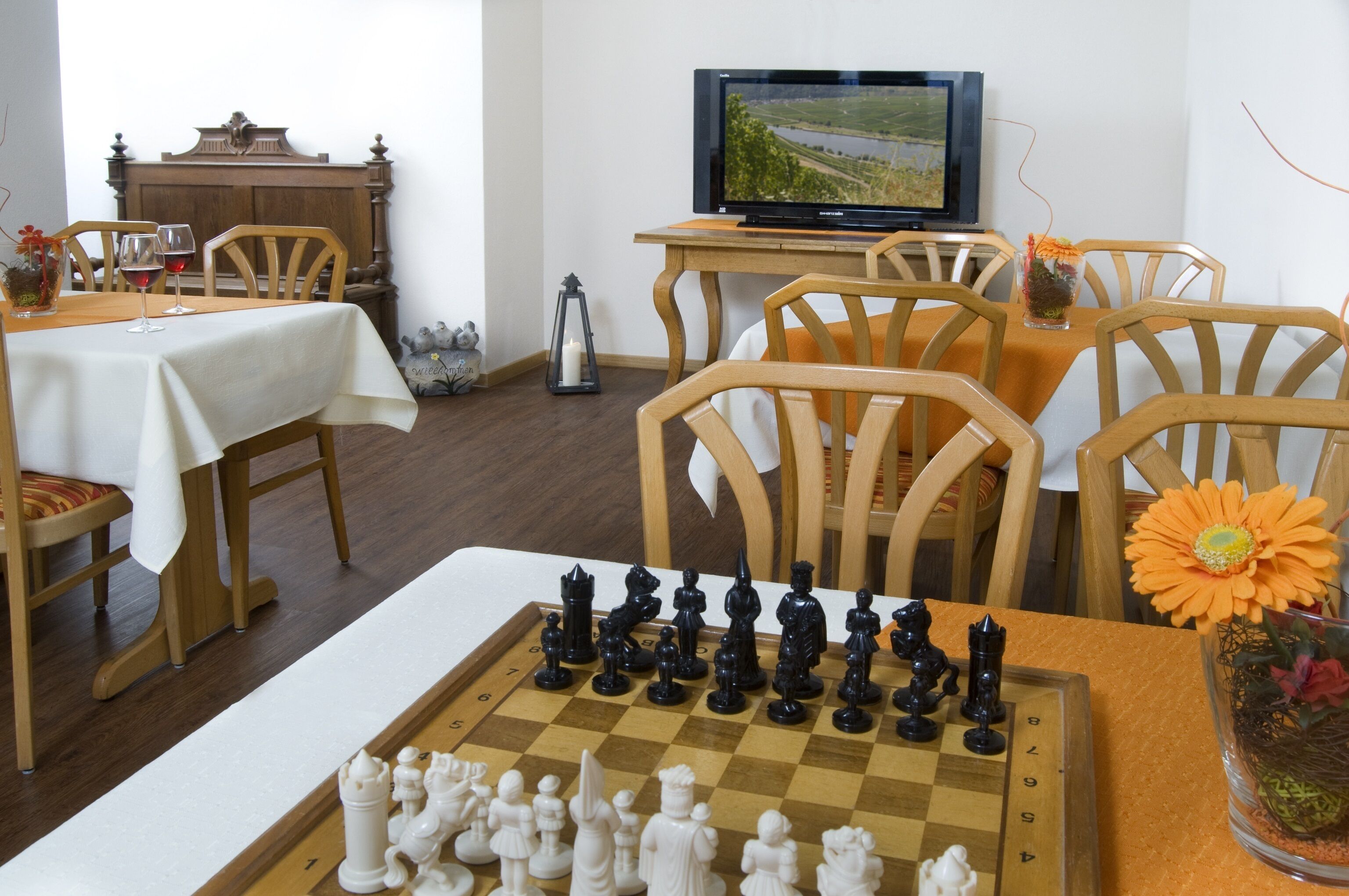 A dining area with a chessboard, wooden chairs, a television, and a table with a white tablecloth.
