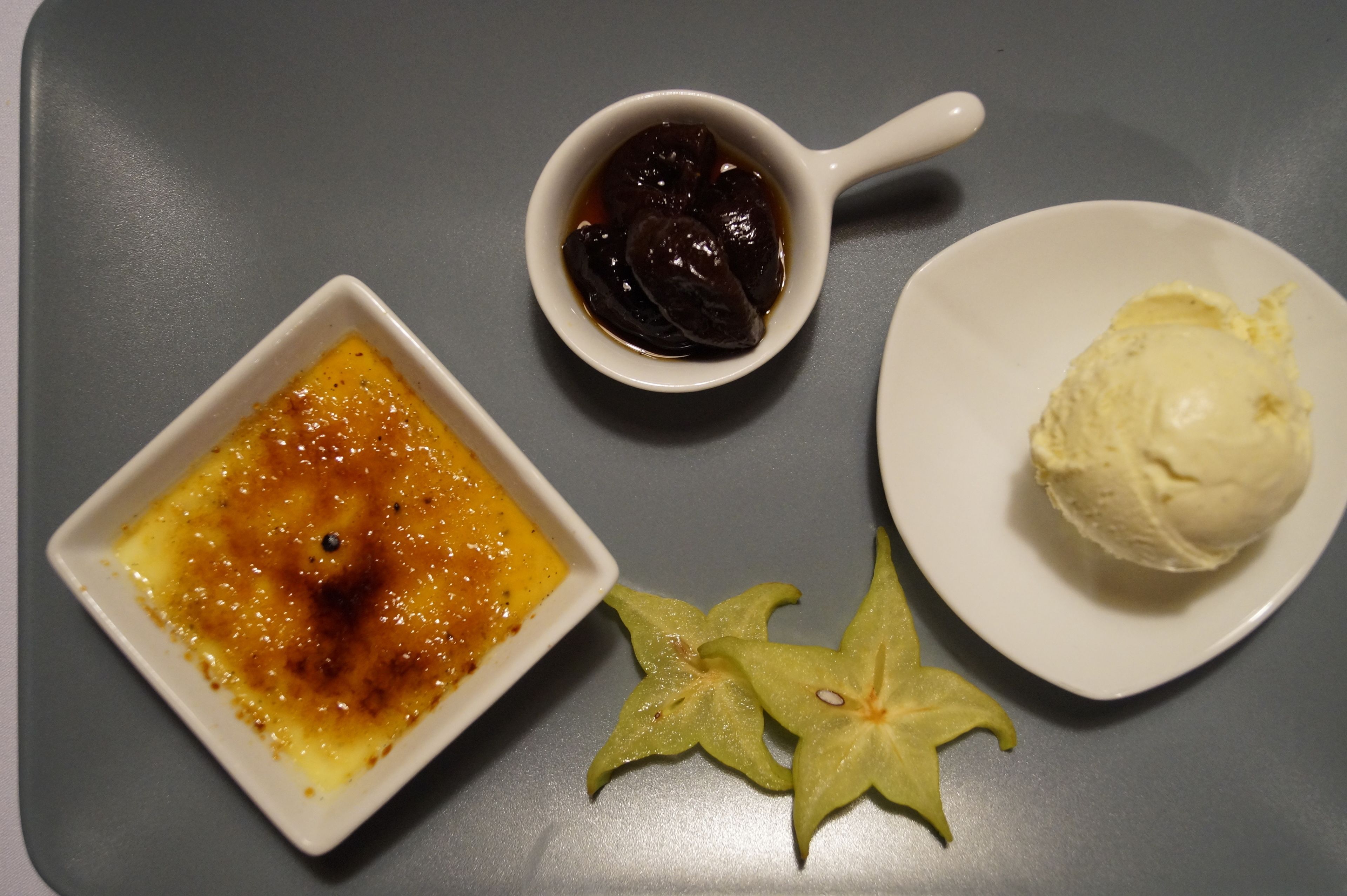 Ein Dessertteller mit Crème brûlée, einer kleinen Marmeladenschale und einer Kugel Eis.