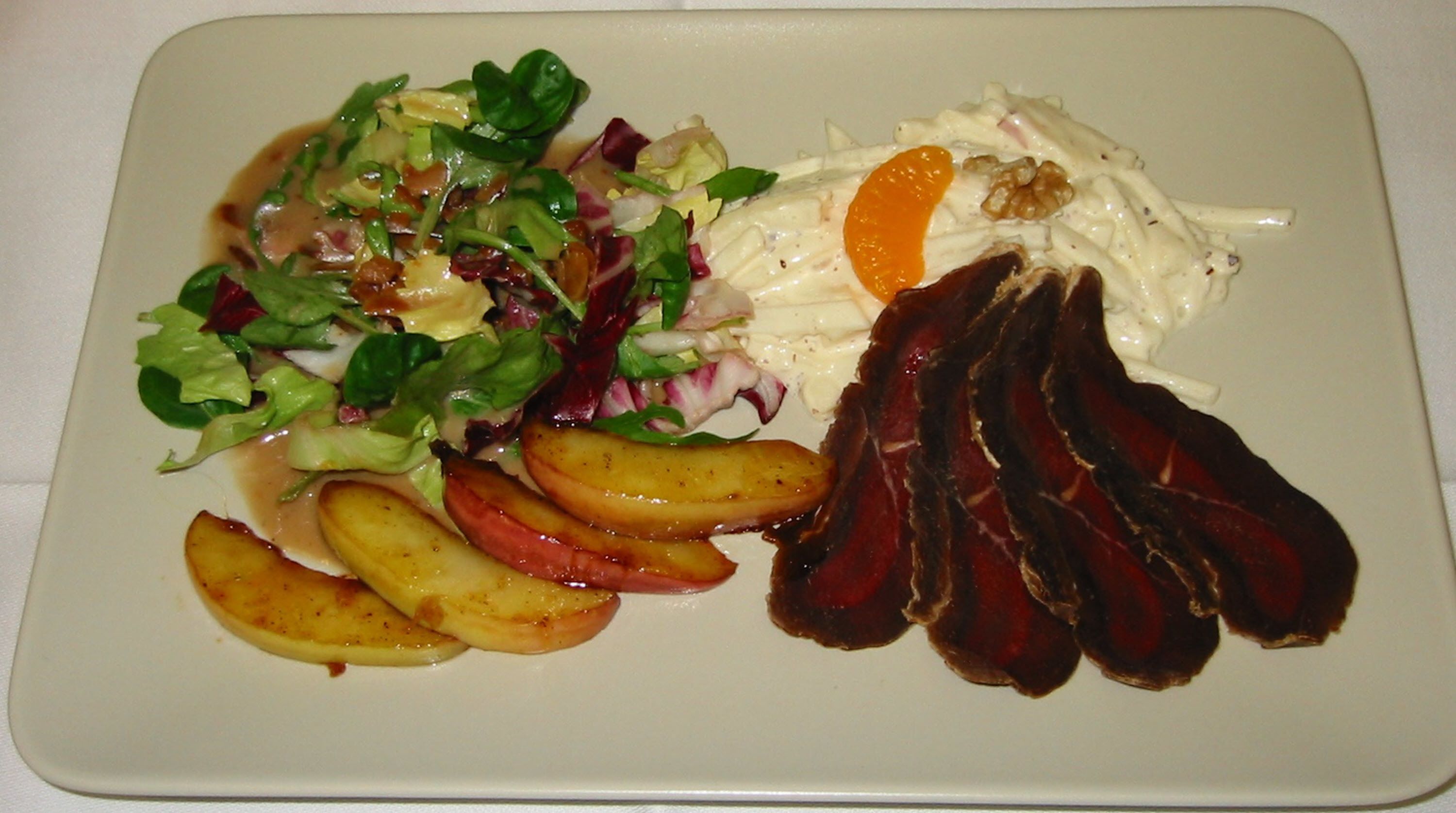 A plate with a salad, roasted potatoes, and slices of meat.