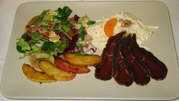 A plate with a salad, roasted potatoes, and slices of meat.