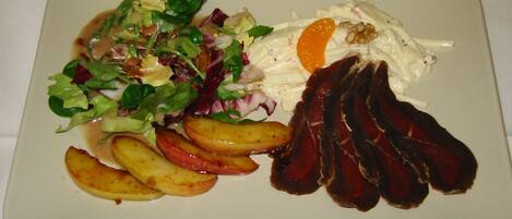A plate with a salad, roasted potatoes, and slices of meat.