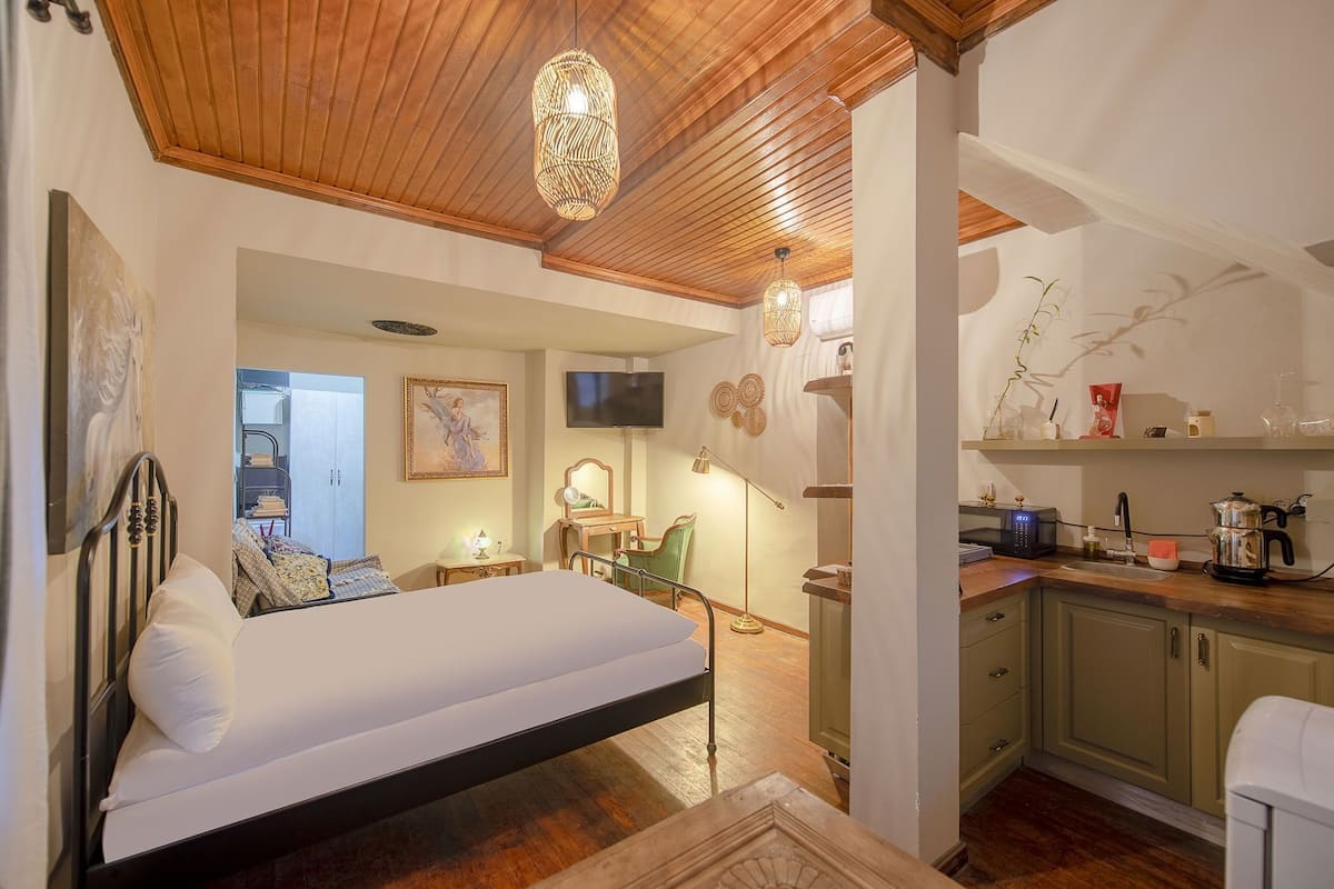 A bedroom with a bed, a desk, a chair, a television, and a kitchen area with a microwave and coffee maker.