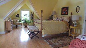 A bedroom with a sloped ceiling, a four-poster bed, a bedside table with a lamp, a small rug, and a potted plant. - Montrose Farms Alpaca Ranch (Brownsburg)