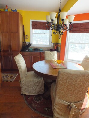 A dining area with a round table, chairs, a chandelier, and a window with blinds. - Montrose Farms Alpaca Ranch (Brownsburg)