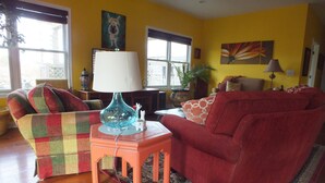 A living room with a red sofa, a multicolored armchair, and a blue lamp on a wooden side table. - Montrose Farms Alpaca Ranch (Brownsburg)
